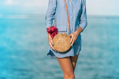 女人穿着蓝白相间的条纹连衣裙衬衫穿着棕色的柳条crossbody袋附近海在白天
